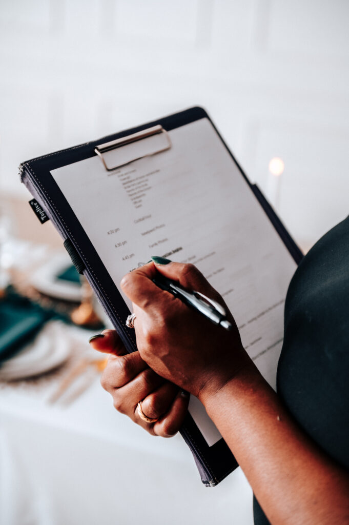 Person holding a clipboard and pen, writing on a document with a table setting in the background.