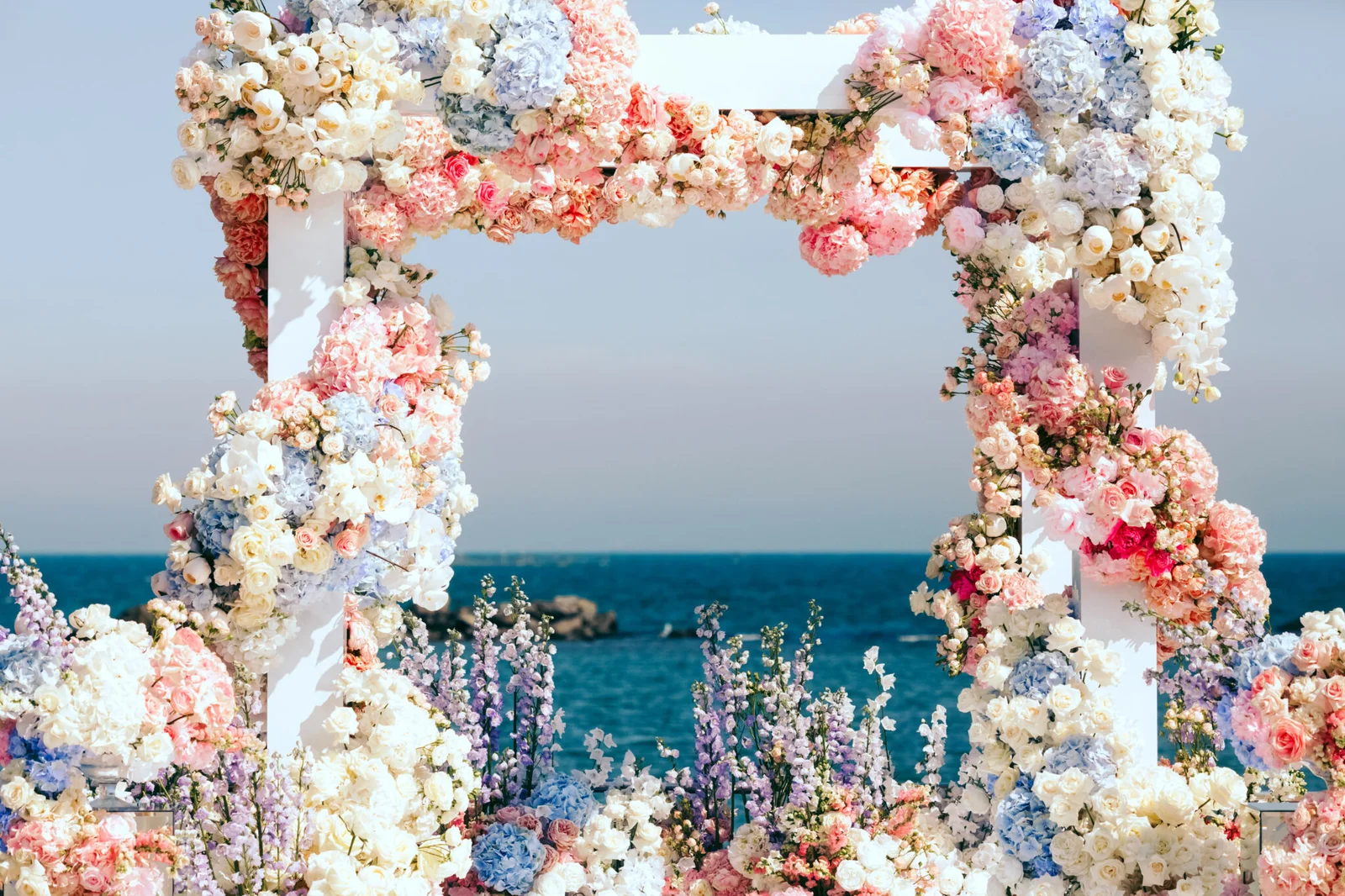 Floral arch with pastel flowers overlooking a calm blue sea under a clear sky